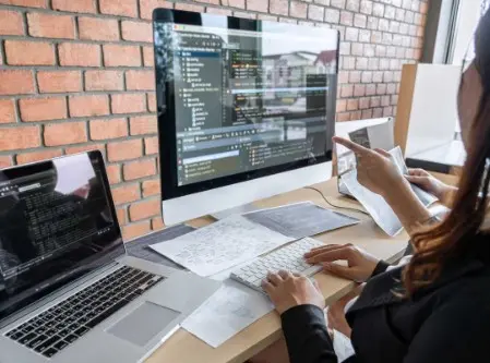 Immagine di una postazione di lavoro con due operatrici davanti ad un Mac e ad un Notebook mentre analizzano dei dati sullo schermo del computer.