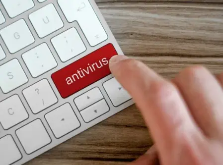 Immagine di un dettaglio di una porzione di tastiera di un notebook con un tasto rosso "antivirus" che sta per venire premuto da un dito di una mano dell'operatore.